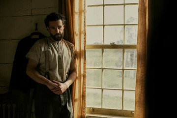 "A man with a beard stands pensively near a sunlit window in a rustic room, dressed in an old-fashioned shirt and trousers. The environment suggests a historical or rural setting with muted colors and a calm mood." "A man with a beard stands pensively near a sunlit window in a rustic room, dressed in an old-fashioned shirt and trousers. The environment suggests a historical or rural setting with muted colors and a calm mood."